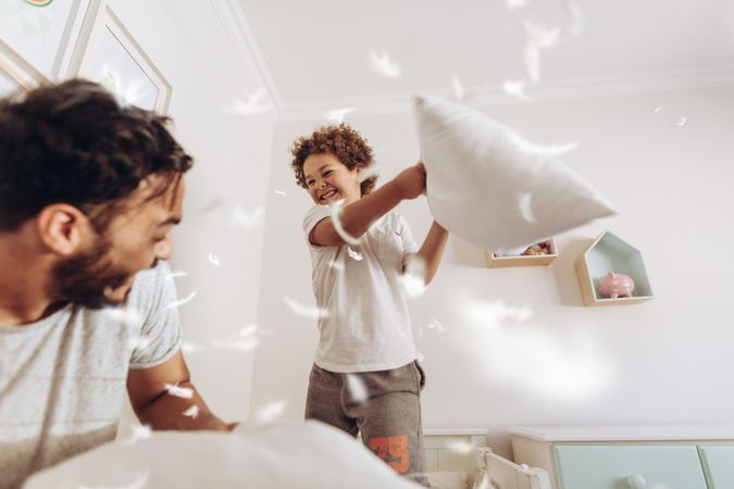 Happy father and son having a pillow fight on bed with feathers flying around