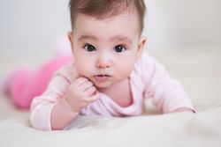 Portrait of baby in pink pajama laying forward on textile