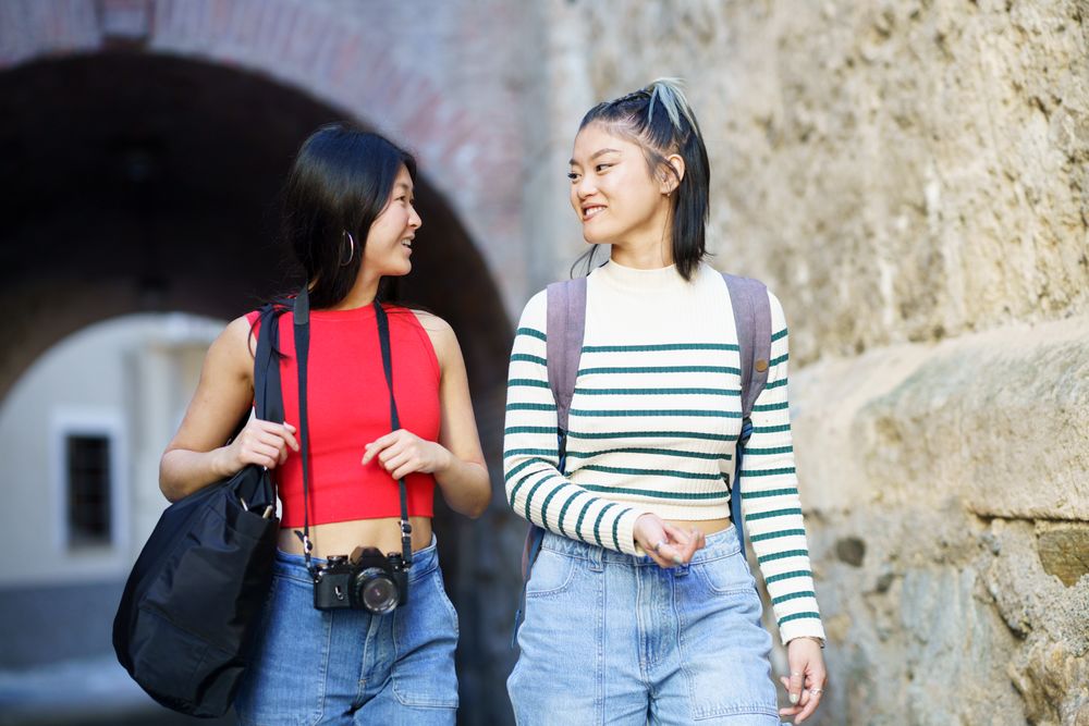 Two women in jeans walking outside with bags and camera