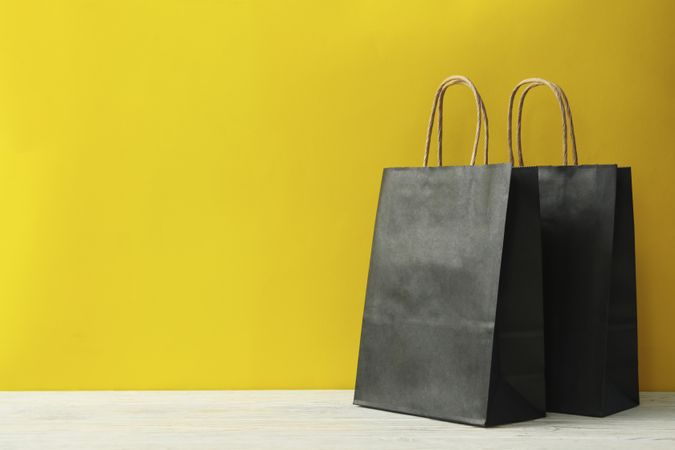 Paper bags on wooden table against yellow background
