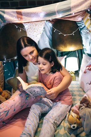 Girl reading with her mother in a makeshift tent