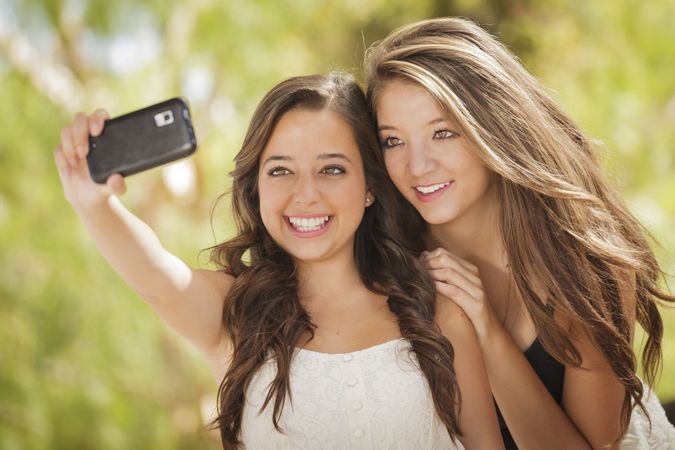 Two smiling female friends taking selfie outside