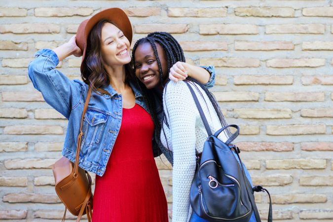 Two women smiling and hugging in front of a brick wall