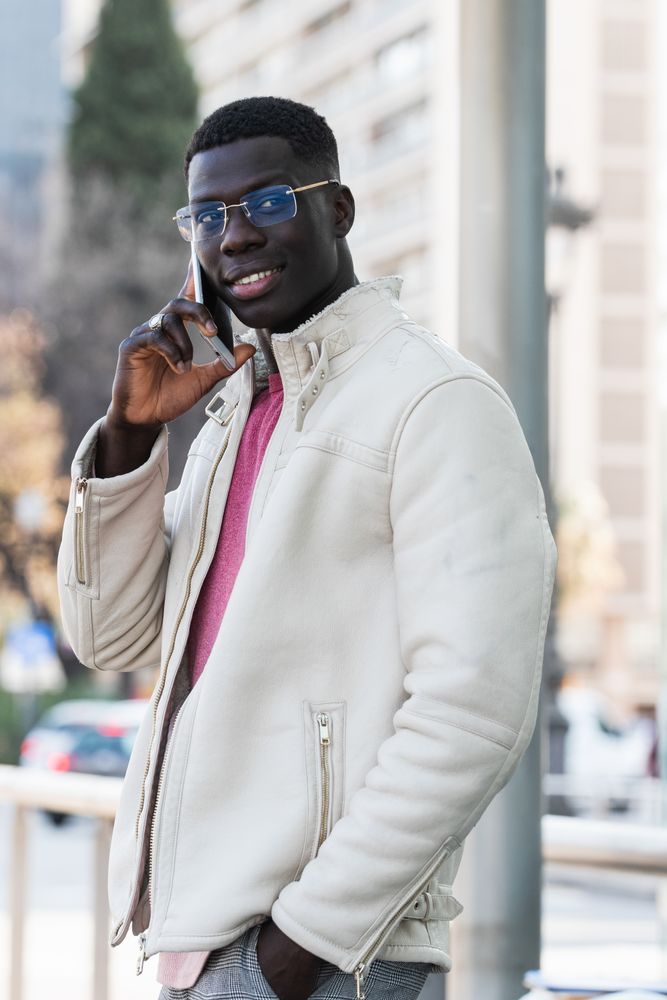 Cheerful Black businessman in eyewear talking on smartphone
