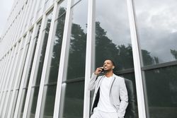 Elegant Black man talking smartphone leaning building