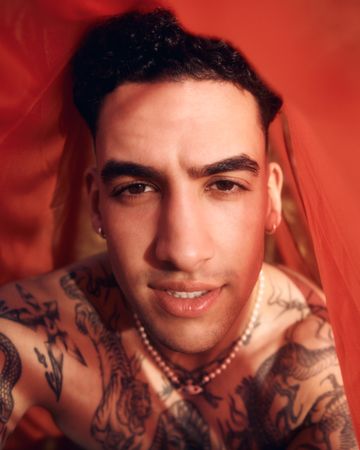 Tattooed male under red sheet, vertical