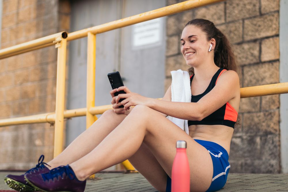 An athletic woman resting with her smartphone after running.