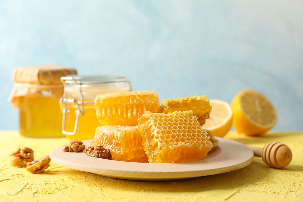 Walnut, honeycombs, jars with honey, dipper and lemon on yellow background, copy space