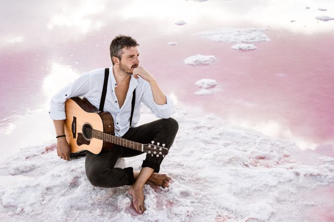 Musician with guitar on pink sandy water