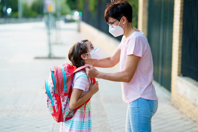 Mother helping young girl with her backpack