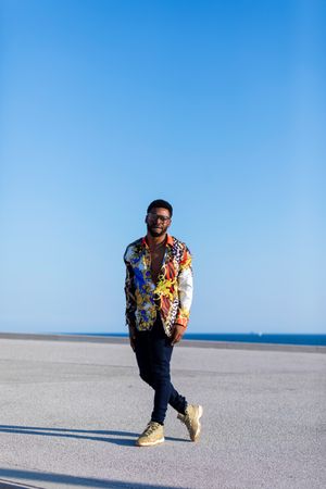 Black man walking while wearing eyeglasses and loud shirt against blue sky on sunny day