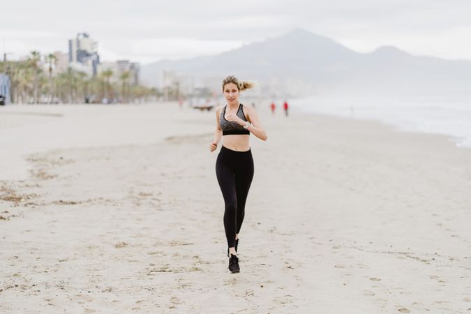 Female runner in stylish sportswear jogging along calm sandy seaside