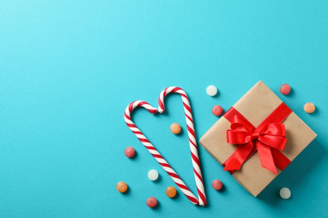 Sweet candy canes and gift box on turquoise background, space for text