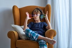 Boy in pajama sitting in armchair and making string figures