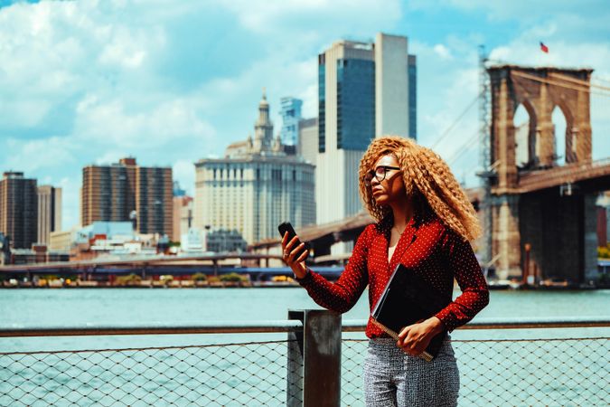Serious professional Black female holding her phone out by Hudson River