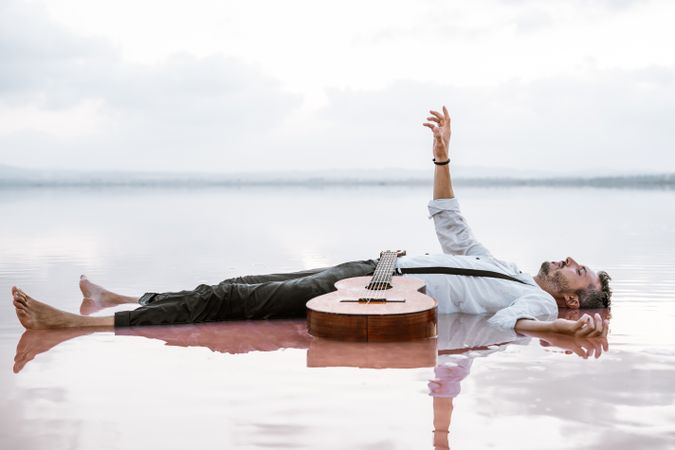 Man resting in water with guitar at seaside