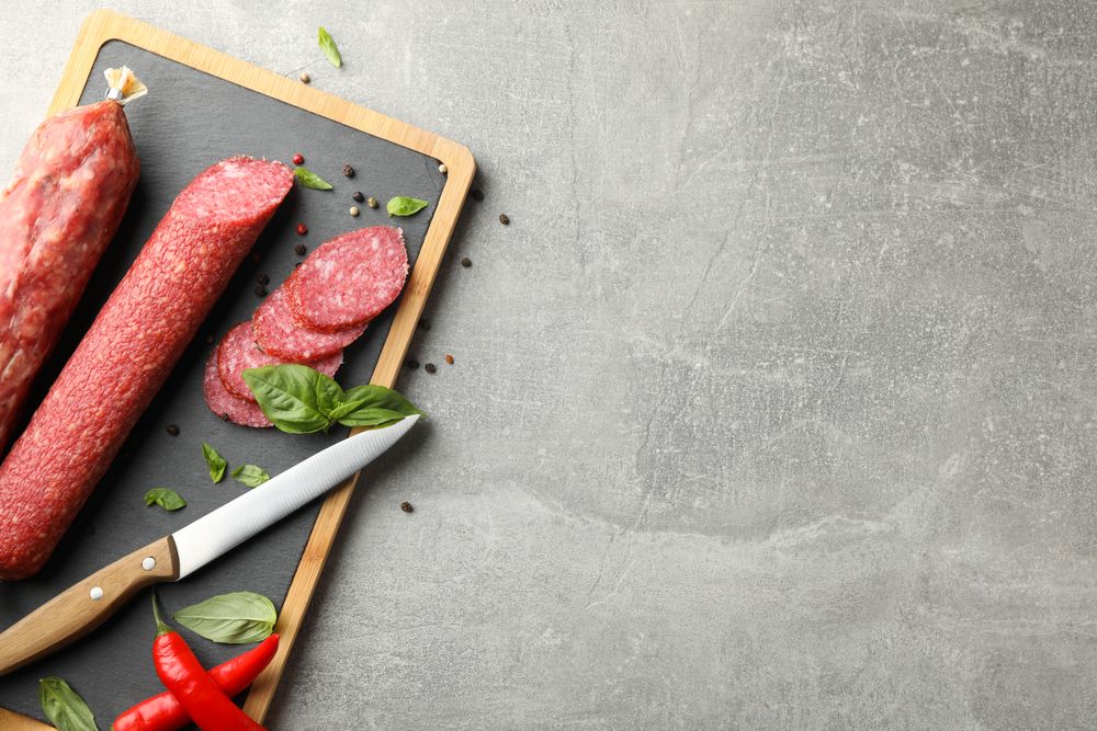 Looking down at two sticks of cured meats with slices on wooden board, copy space