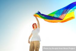 Young woman waving rainbow flag under blue sky 4ZMZy5