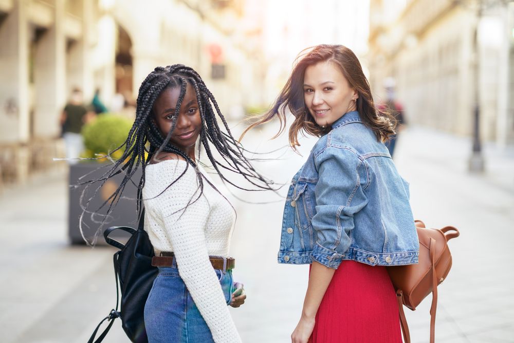 Two female friends walking on a sunny outdoor street while looking back