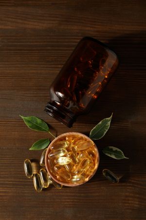 Wooden bowl with omega pills on dark background