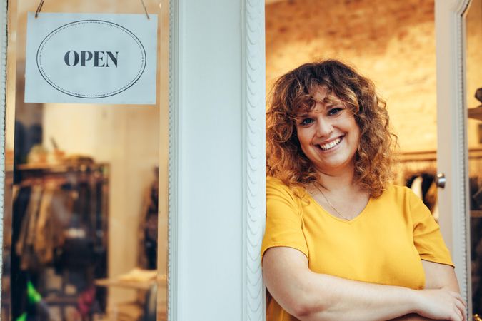 Portrait of a clothing store owner standing at the door with open sign