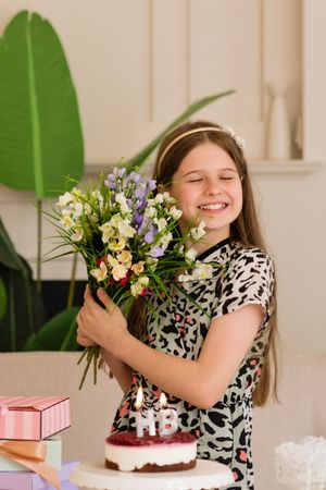 Girl holding flowers and closing eyes at birthday party.