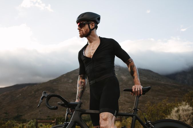 Muscular cyclist with a road bike standing on countryside road