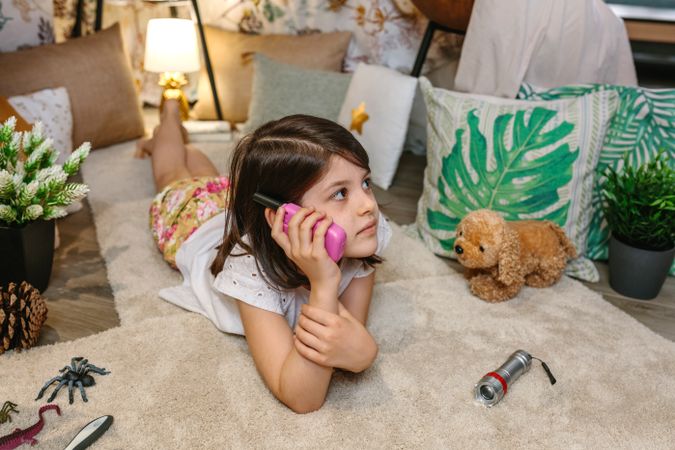 Portrait of girl using walkie-talkie lying over rug surrounded by cushions and plants in teepee