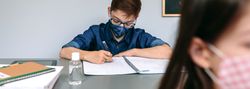 Boy with face mask writing at school