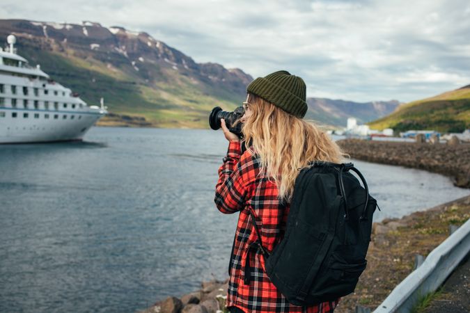 Woman with backpack takes photo of cruise ship in port