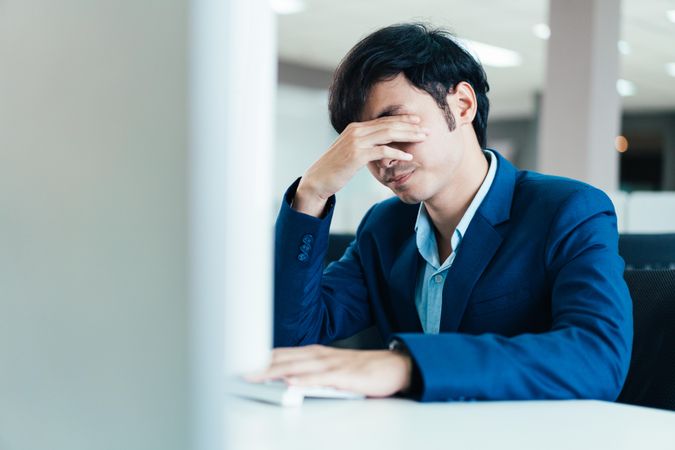 Stressed Asian male in suit in his office