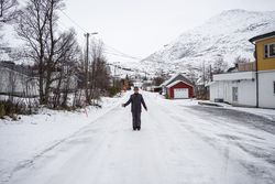 Solitary old man on empty street in small town against snowy hillside