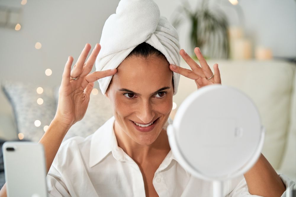 Cheerful woman doing face massage looking at mirror