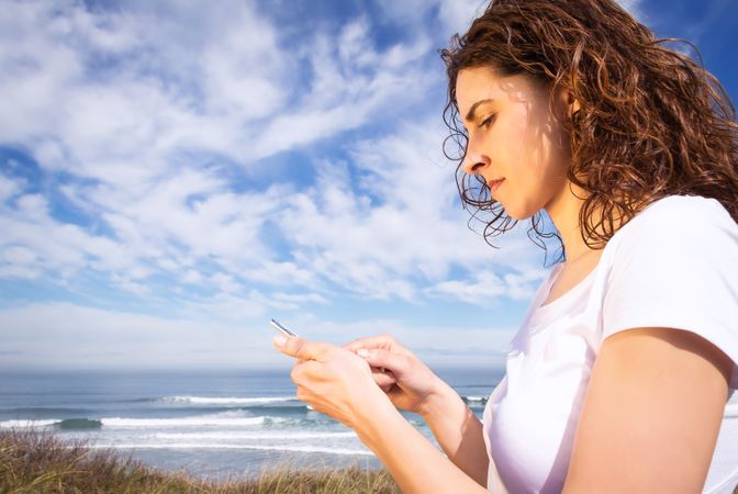 Woman in t-shirt checking phone with ocean waves in background