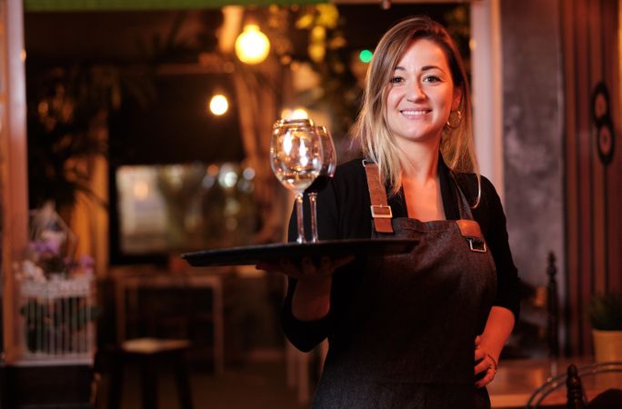 Cheerful waitress holding tray with wineglasses