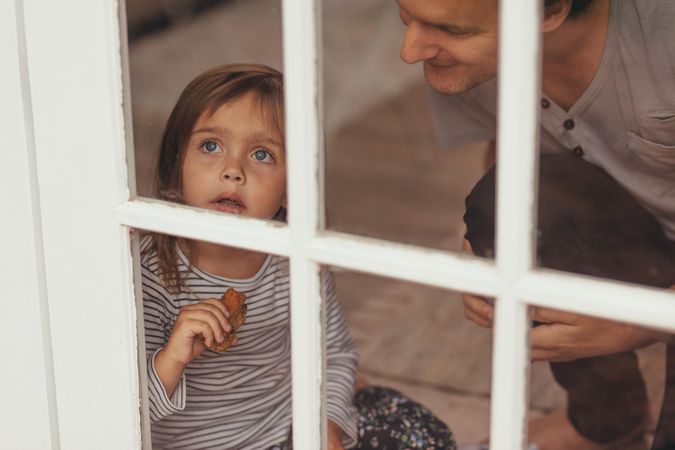 Little girl sitting beside a window and looking outside holding a piece of cake
