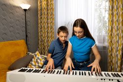 Two children play digital piano together in cozy living room.