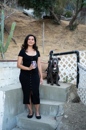 Full length portrait of woman standing and smiling at camera with dog sitting next to her