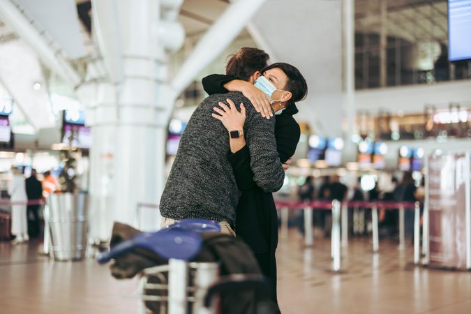 Female wearing face mask welcoming her man at airport arrival