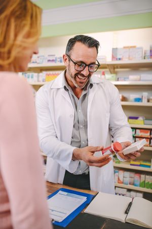 Professional male pharmacist showing medicine to female customer in pharmacy