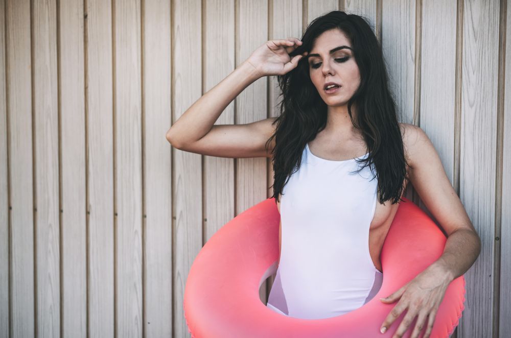 Woman with a swimming ring posing by white wooden fence
