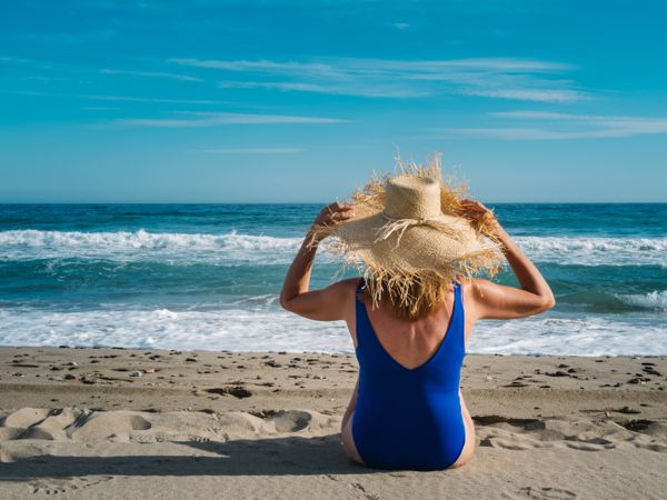 Woman in blue swimsuit and hat on sandy beach