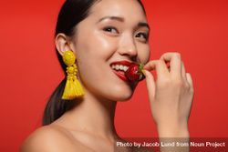 Female model with long earring and eating strawberry against  red background 5qqjj5