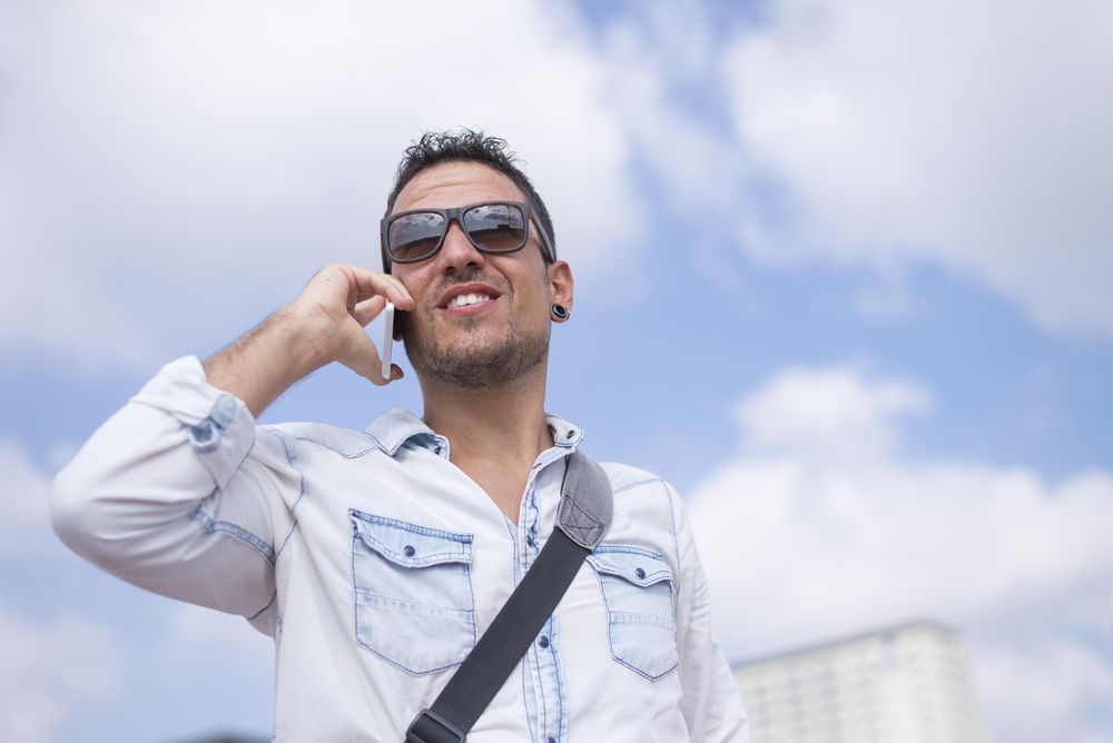 Happy male having conversation on cell phone with sky in background