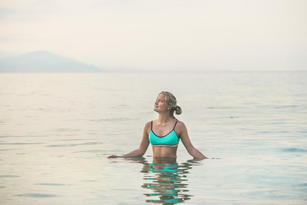 Blonde woman in bright bikini top standing waist deep in sea