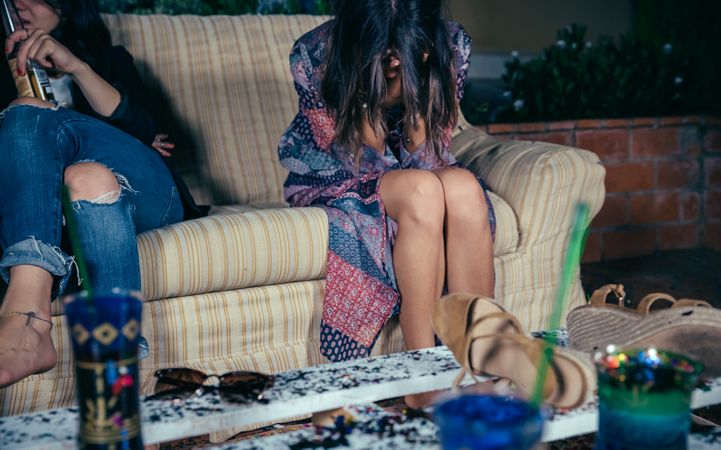 Young drunk woman sitting with her head in her hands on a sofa at party