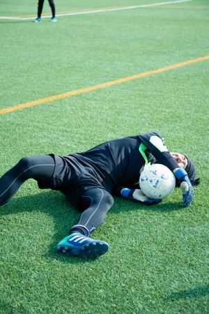 Injured football player laying on green grass with the ball