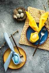 Top view of Easter holiday table setting with yellow & blue egg decoration in bunny napkin on plate