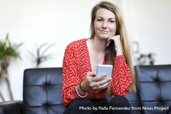 Blonde woman using a smartphone while sitting on leather sofa 0v3Gno