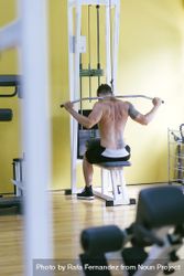 Tattooed male exercising his arms and back on pull down machine, vertical 4Om7E0